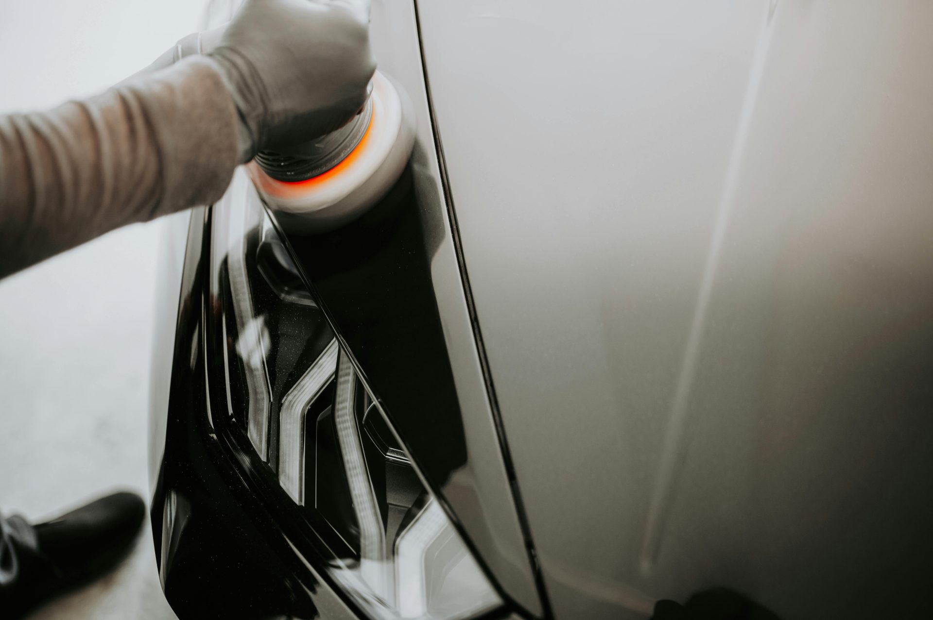 Primer plano de una persona puliendo un coche negro con una máquina pulidora.