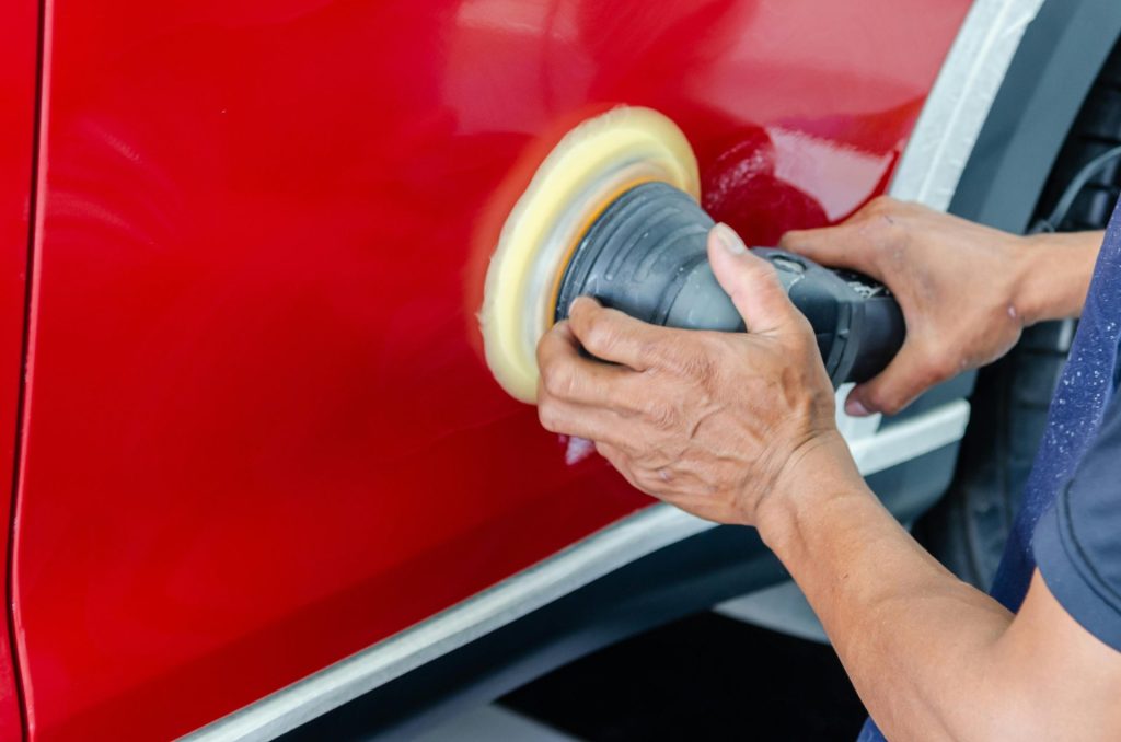 Primer plano de un trabajador puliendo la pintura roja de un coche para darle brillo y mantenerla en buen estado.